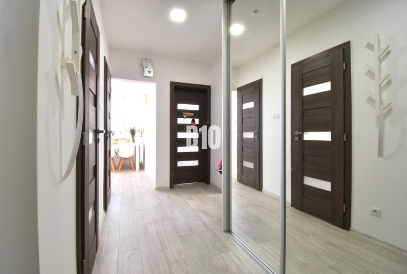 A hallway in a 3-room apartment with a mirrored wardrobe and a wooden decor floor.