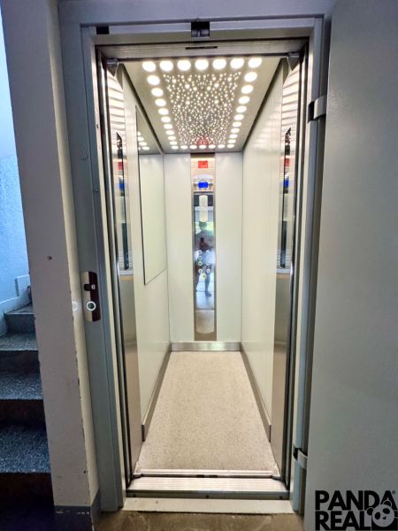 An elevator with an illuminated ceiling and light walls in a residential building.