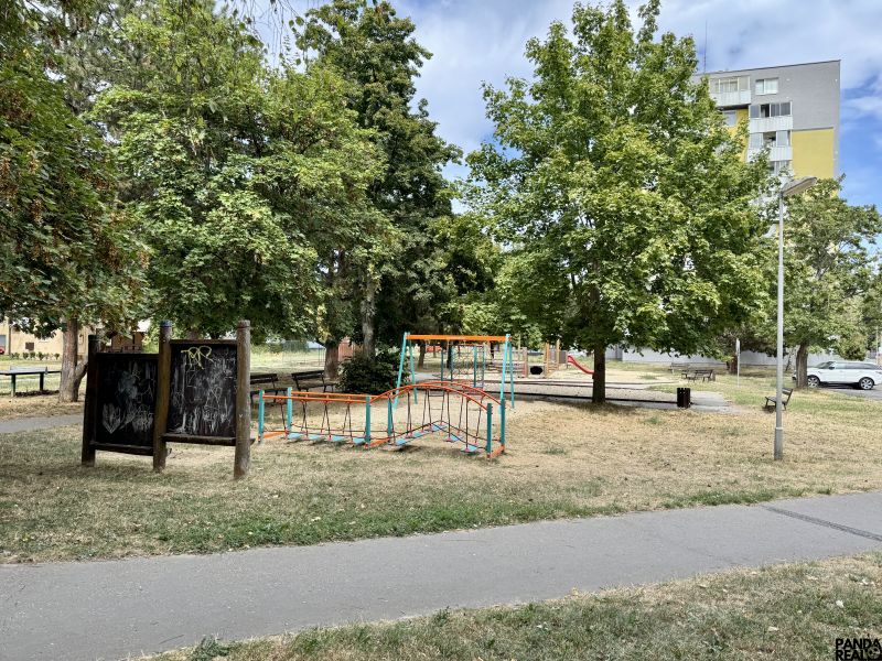 A children's playground surrounded by trees in a park in the town of Topoľčany near a one-bedroom apartment.