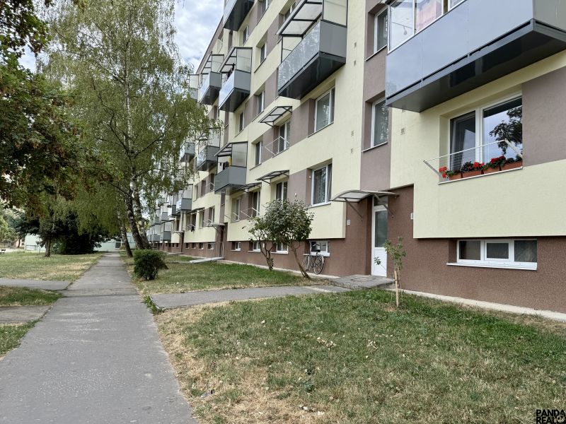 An apartment building with greenery and a walkway, located in Topoľčany, surrounded by trees.