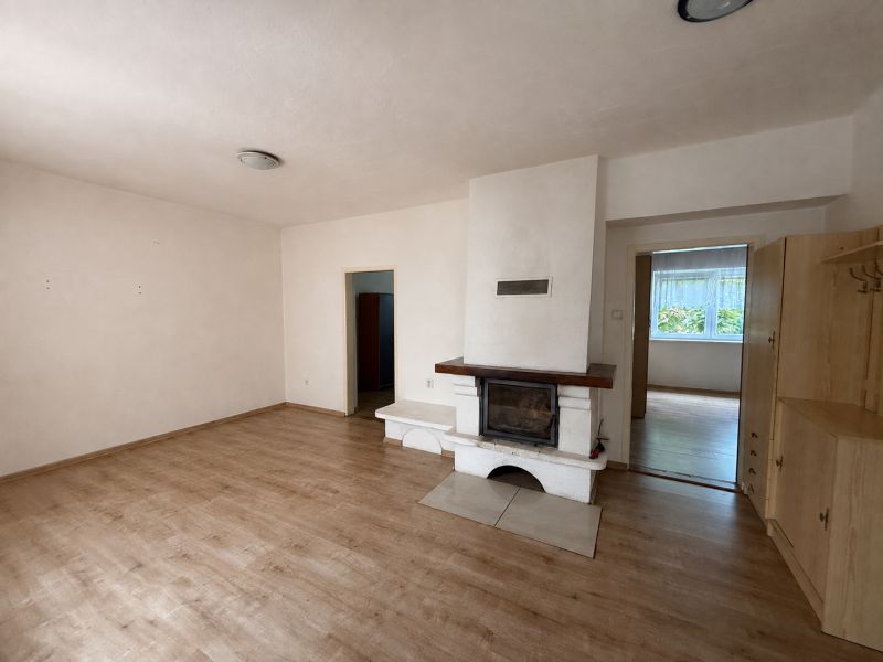 Interior of a family house with a fireplace, wood-patterned flooring, and simple furnishings.
