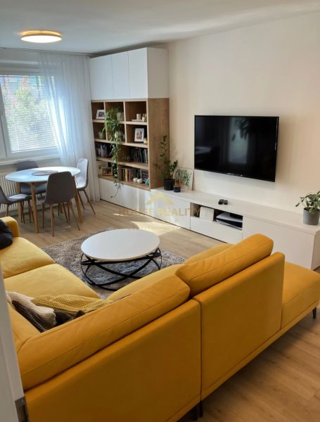 Living room in a 3-room apartment with a comfortable sofa, dining table, and wooden decor flooring.
