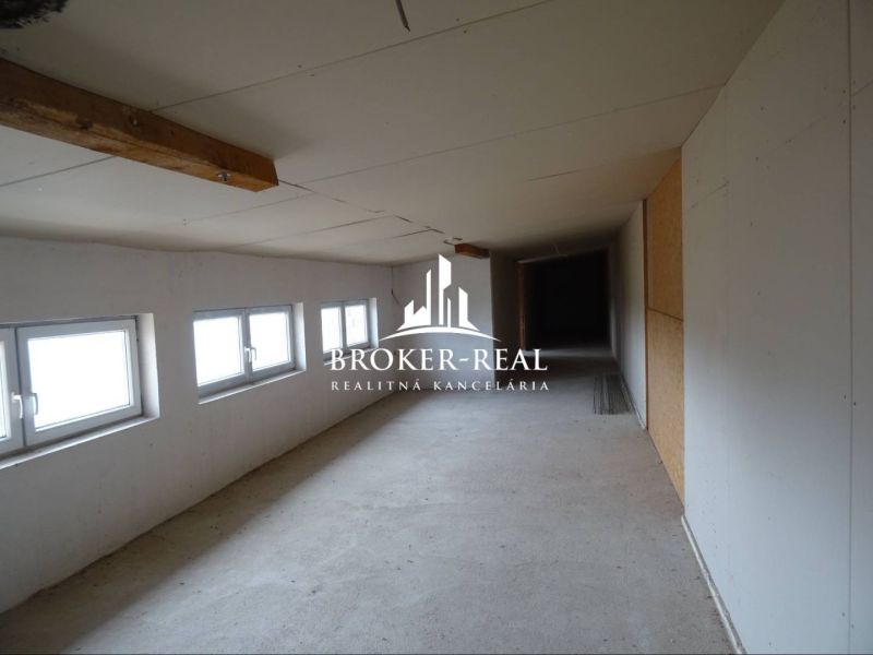 A narrow interior of a warehouse with white walls and a row of windows on the left side.