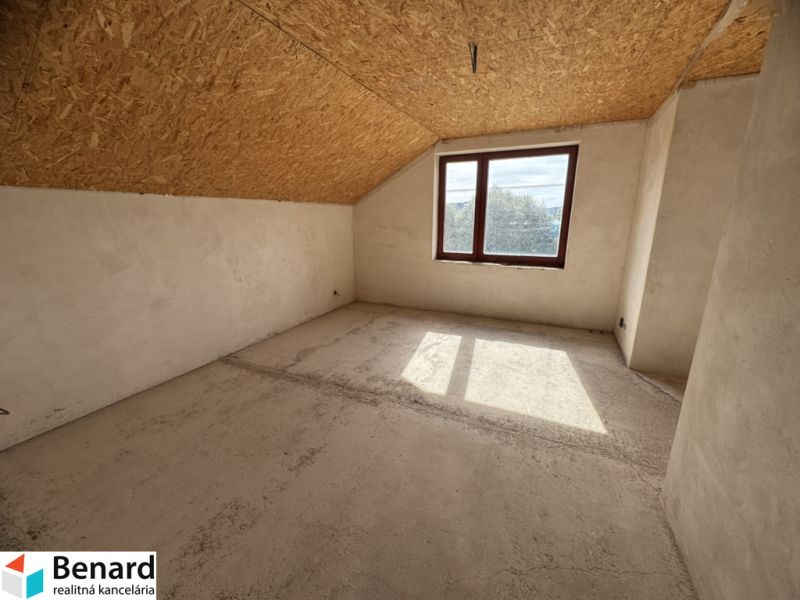 The interior of a family house with a window, slanted ceiling, and unfinished floor.