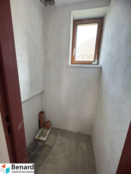 A small room with a window in a family house, unpainted walls, tiled floor.