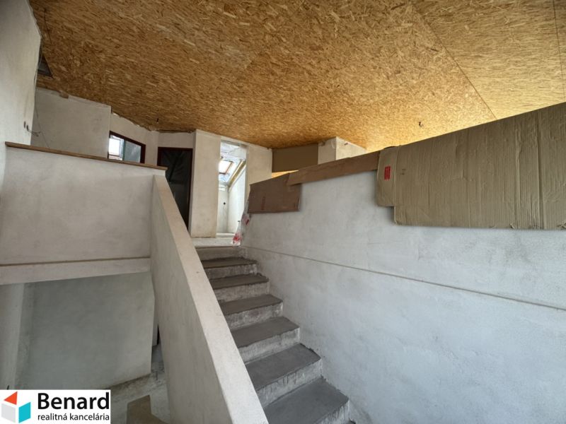 Interior of a family house with a staircase, white walls, and OSB boards on the ceiling.