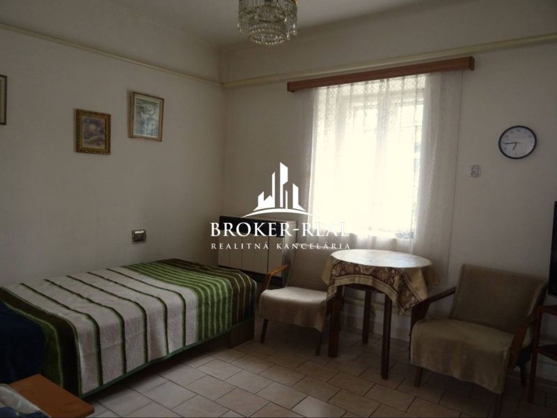 A room in a family house with a bed, chairs, and a table, decorative paintings on the wall.