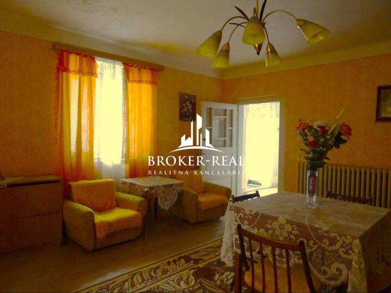 A living room in a family house with orange curtains and a table with a tablecloth.