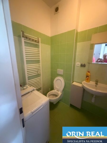 A studio apartment bathroom with green tiles, a sink, a toilet, and a washing machine.