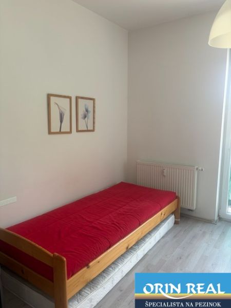 Studio apartment with a bed, red blanket, and wooden decor flooring.