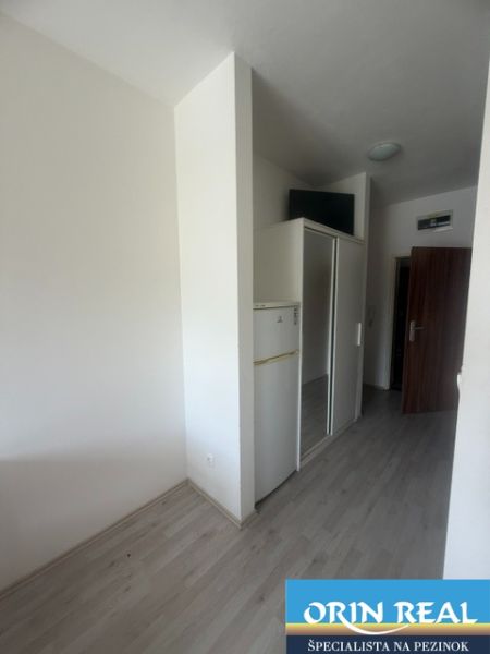 Studio apartment with wood-patterned flooring, a refrigerator, and a built-in wardrobe.