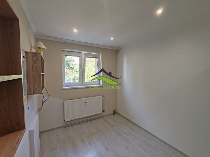 A room in a 3-room apartment with a wooden decor floor, a wall lamp, and a radiator.