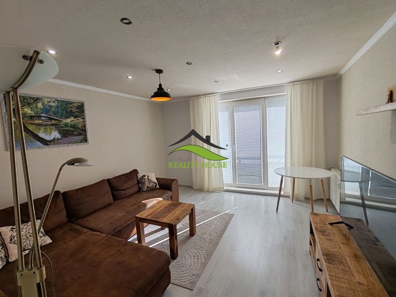 A living room in a three-room apartment with a wooden decor floor and a brown sofa.