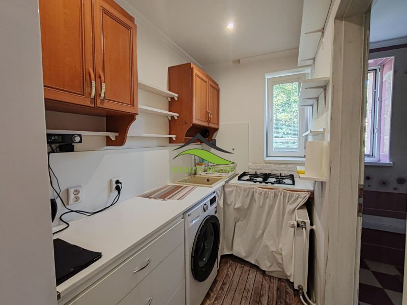 A kitchen in a 3-room apartment with wood-patterned flooring, a washing machine, and upper cabinets.