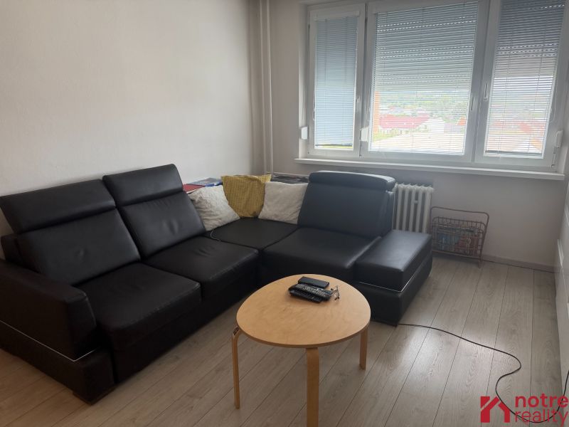 Living room in a two-room apartment with a black couch and a floor with a wood decor.