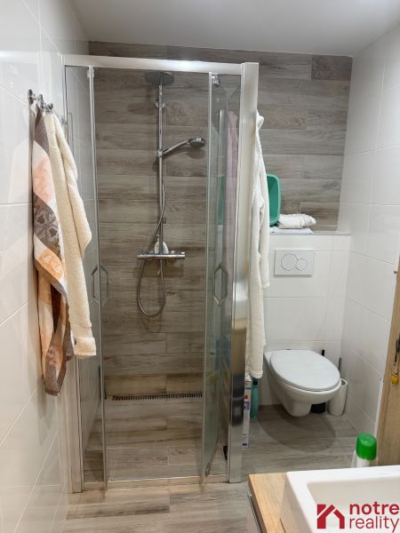 Bathroom in a 2-room apartment with a wooden decor floor and a shower corner.