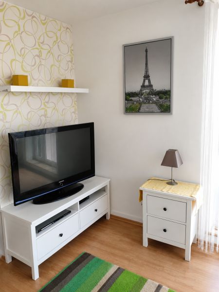 Living room in a two-room apartment with a wooden decor floor, a television, and a table.