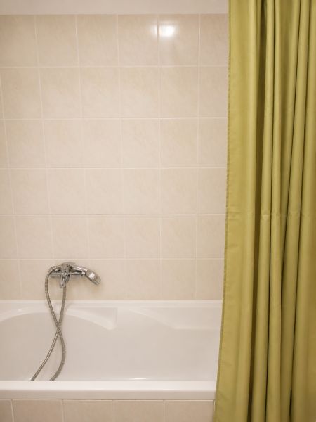 Bathroom with a bathtub, shower curtain, and light tiles in a 2-room apartment.