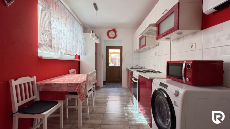 A kitchen in a family house with a table, chairs, appliances, and red details.