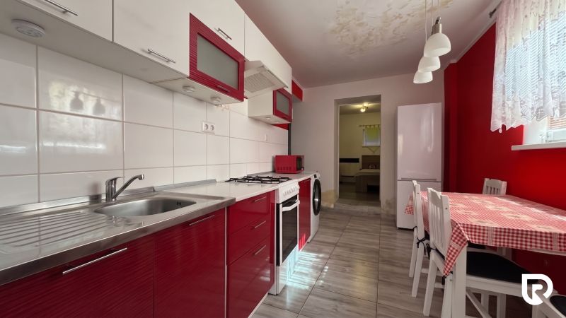 A kitchen in a family house with red cabinets and a dining table with a checkered tablecloth.