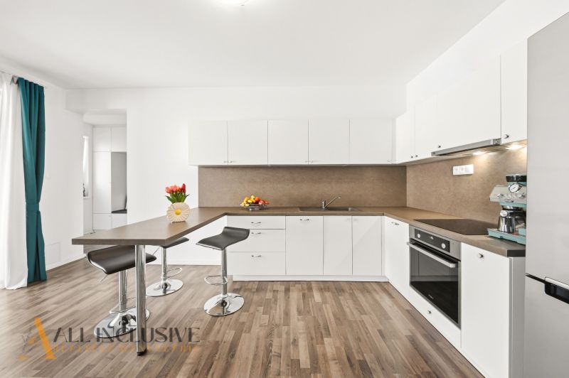 A kitchen with white cabinets, a colorful table, and a wood-patterned floor in a three-room apartment.