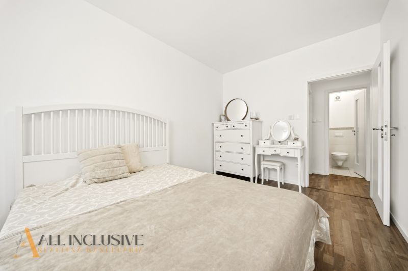 A bedroom in a three-room apartment with a bed, a dresser, and a floor with a wood decor.