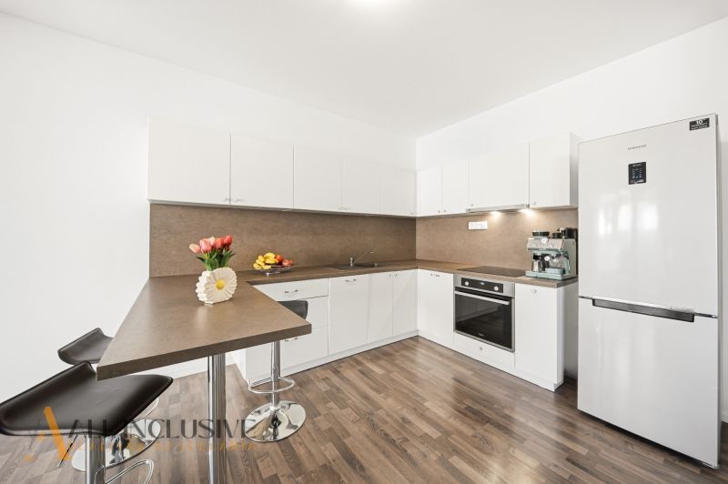 A kitchen in a 3-room apartment with light furniture, a bar counter, and a floor with a wooden decor.