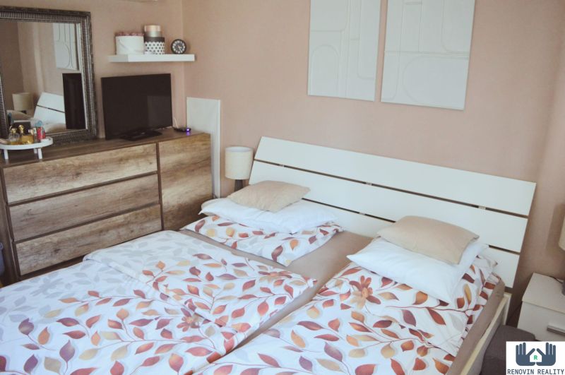 Bedroom in a 3-room apartment with a bed and a dresser with a wood-patterned floor.