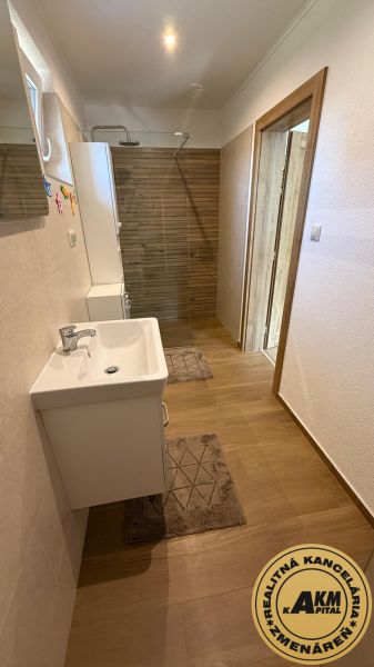 A bathroom in a family house with a sink, a shower corner, and a floor with a wooden decor.