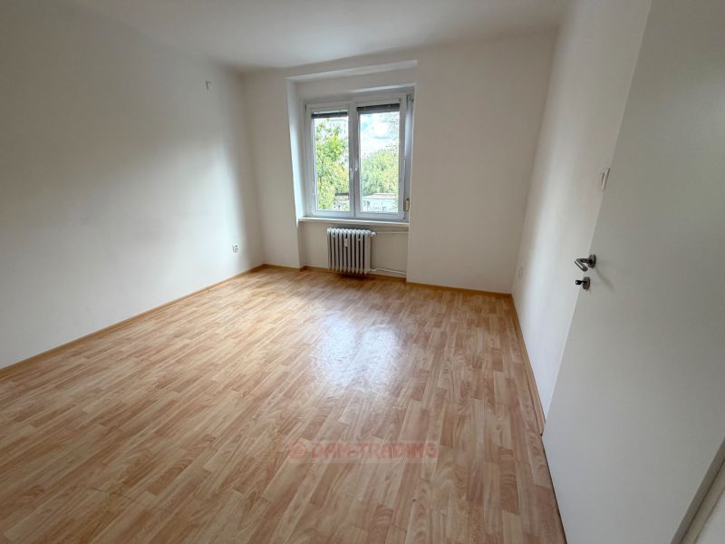 A room in a two-room apartment with a wooden decor floor and a large window.