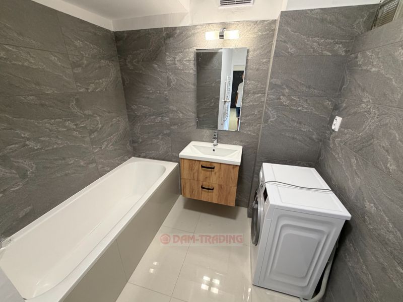 A bathroom with a bathtub, sink, washing machine, and gray walls in a 2-room apartment.