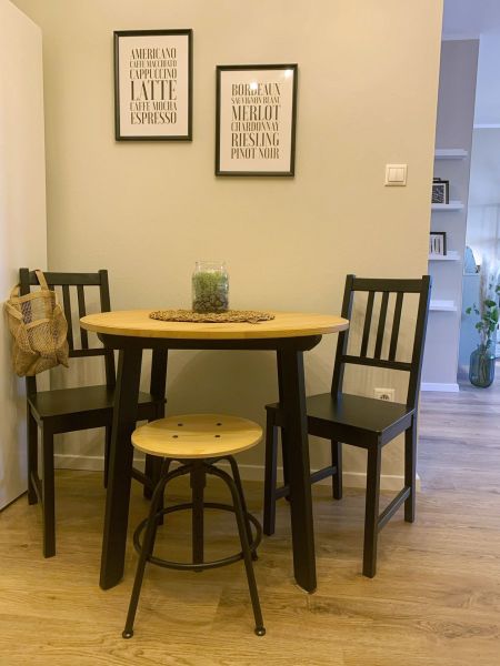 Dining nook in a 2-room apartment with black chairs and a table on a floor with a wooden decor.