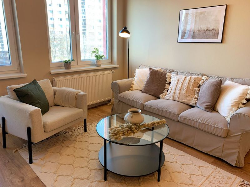 Living room in a 2-room apartment with a gray sofa, an armchair, and a wooden decor floor.
