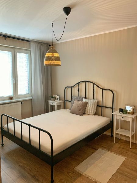 Bedroom in a 2-room apartment with a metal bed and wood-patterned flooring.