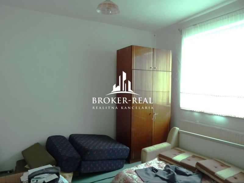 A room in a family house with furniture and a large window provides comfortable seating.