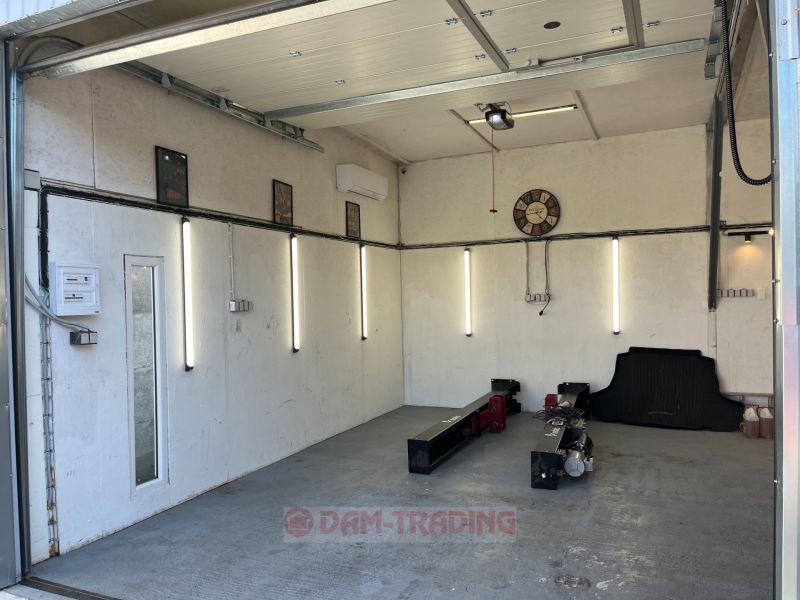 An empty garage with lighting, a garage door, a clock, equipment on the floor of the garden.