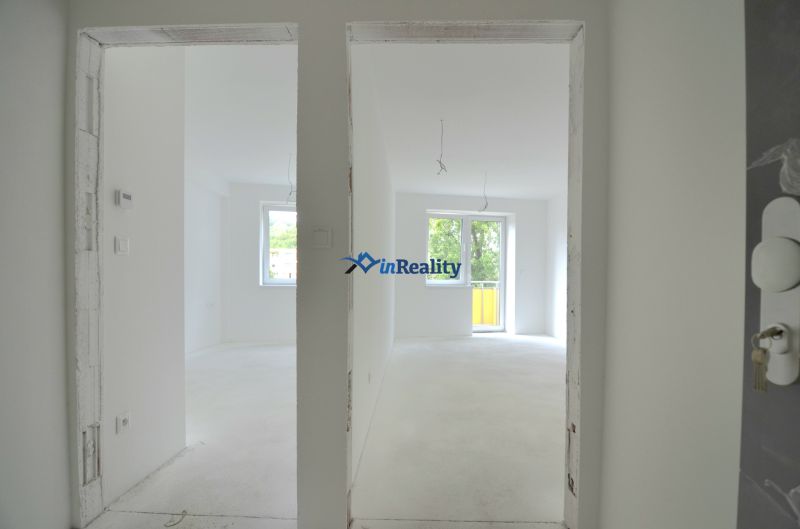 A white interior of an empty 2-room apartment with a window and balcony doors.