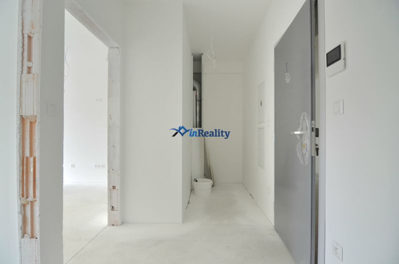 A hallway in a 2-room apartment with a concrete floor and open doors.