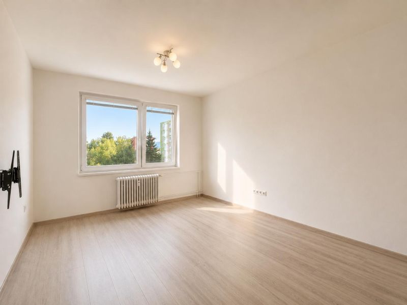 A spacious room with a wooden decor floor, a large window, and a radiator in a 2-room apartment.