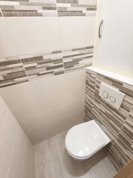 A toilet in a 2-room apartment with light tiles and practical storage space.