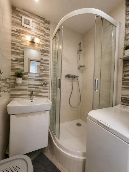 A bathroom with a shower, sink, and washing machine in a 2-room apartment.