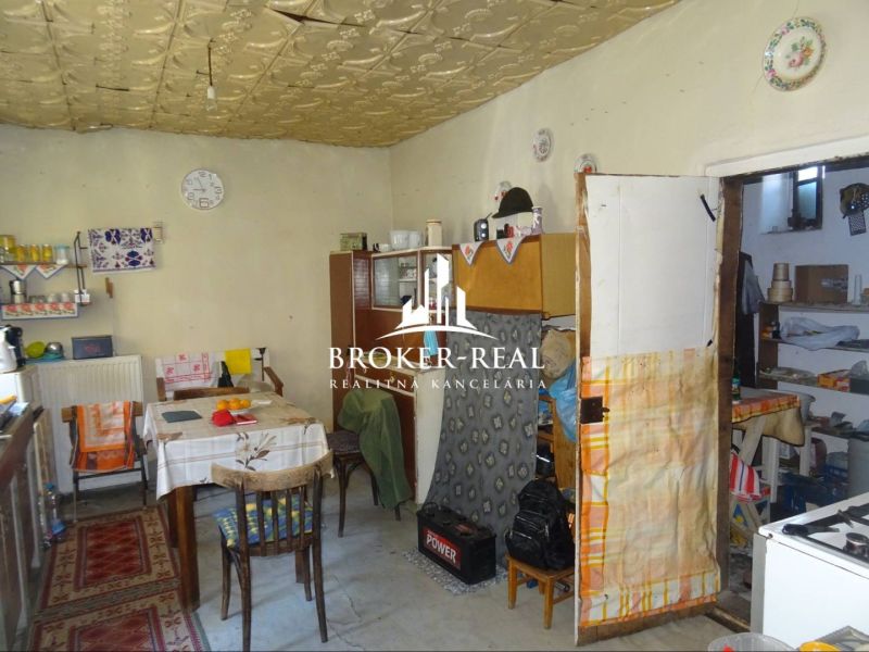 A kitchen in a family house with old equipment, a dining table, and patterned carpets.