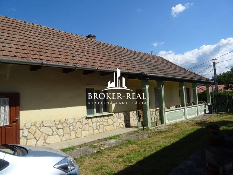 A family house in Abaujvár with stone cladding and a front garden under a blue sky.