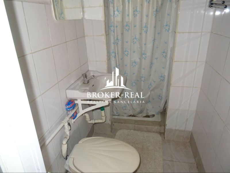 A bathroom in a family house with white tiles, a shower, and a sink.