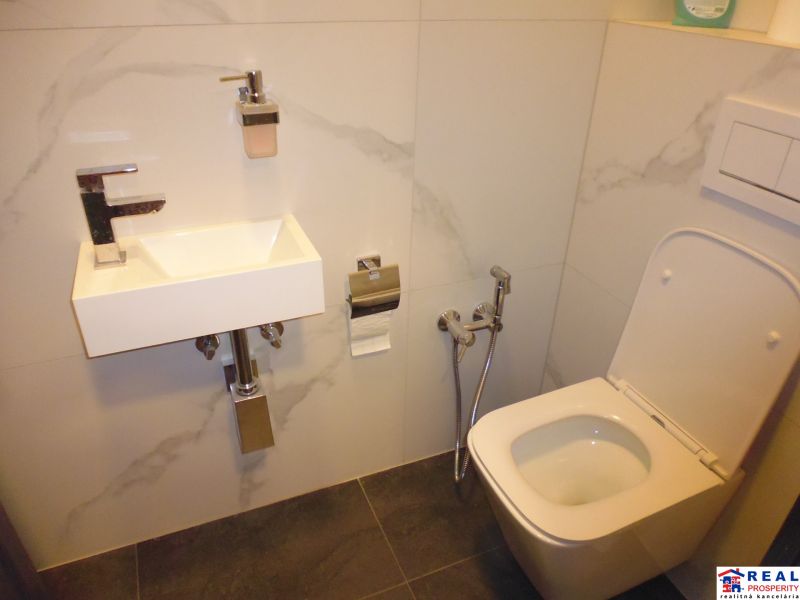 Bathroom with a toilet and a sink, tiled with light tiles.
