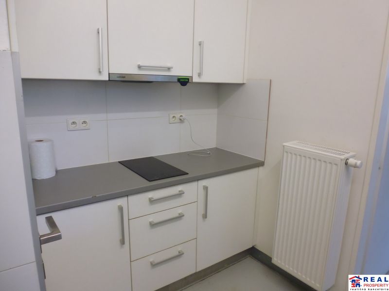 A small kitchen area with white cabinets, a gray countertop, and a radiator.