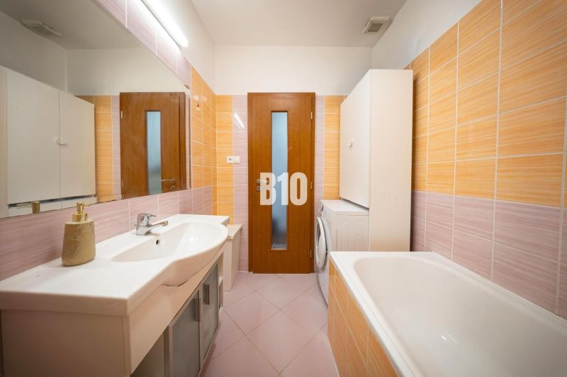 Bathroom in a 2-room apartment with light tiles, a bathtub, and a washing machine.
