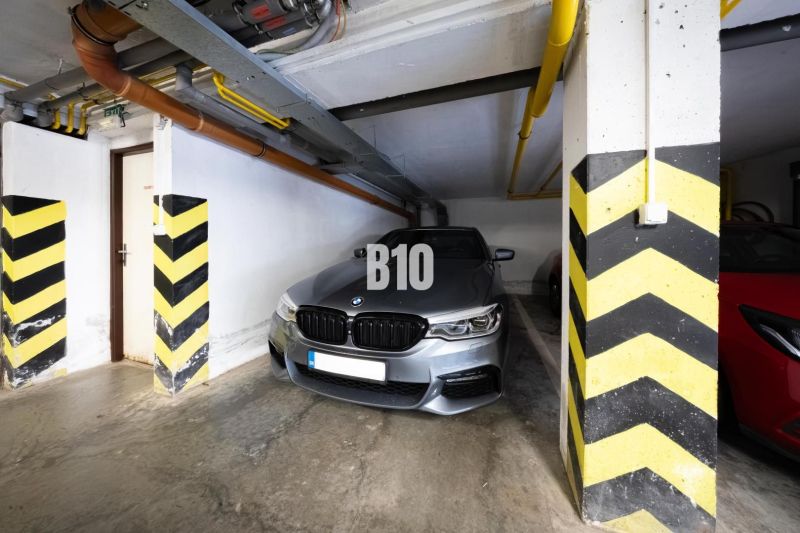 A garage parking space for a car with striped pillars and pipes on the ceiling.