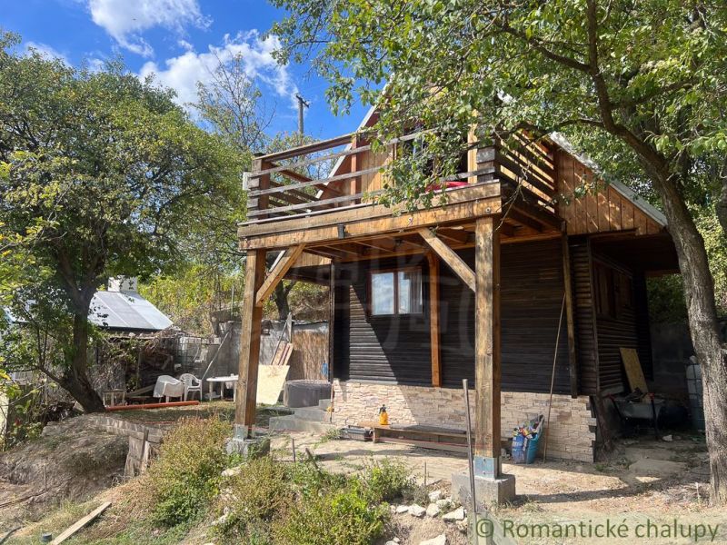 A cottage in Bratislava IV surrounded by trees, wooden balcony, summer day.