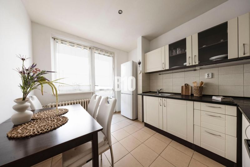 A kitchen in a 3-room apartment with a dining table, white cabinets, and a large window.